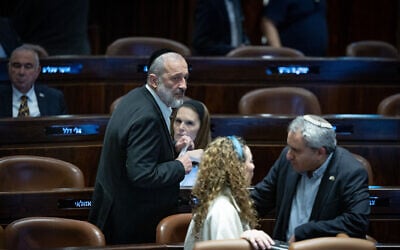 Shas leader Aryeh Deri, left, walks by Ze'ev Elkin, right, in the Knesset plenum on December 25, 2023. (Yonatan Sindel/ Flash90)
