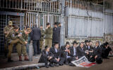Illustrative: Ultra-Orthodox men after clashes during a protest outside the army recruitment office in Jerusalem, as a group of soldiers stands behind them, March 4, 2024 (Chaim Goldberg/Flash90)