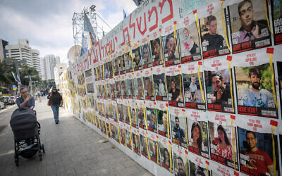 People walk by photographs of Israelis still held hostage by Hamas terrorists in Gaza, at Hostages Square in Tel Aviv. March 14, 2024. (Miriam Alster/FLASH90)