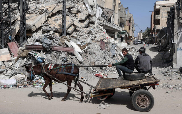 Palestinian boys ride a donkey-pulled cart near a building destroyed in Israeli bombardment in Rafah in the southern Gaza Strip on March 31, 2024. (MOHAMMED ABED / AFP)