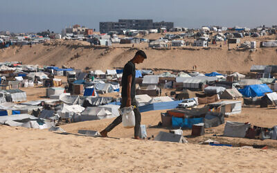 A Palestinian man ferries water at a makeshift camp for displaced people in Rafah in the southern Gaza Strip on April 4, 2024 (Mohammed Abed/AFP)