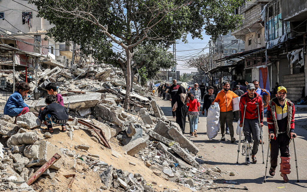 Injured men walk with crutches past children sitting atop the rubble of a collapsed building along a street in Rafah in the southern Gaza Strip on April 9, 2024. (AFP)