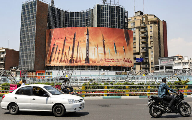 Motorists drive past a billboard showing named Iranian ballistic missiles, with text in Arabic reading, 'The honest [person's] promise,' and in Persian, 'Israel is weaker than a spider's web,' in Valiasr Square in central Tehran, on April 15, 2024. (ATTA KENARE/ AFP)