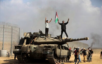 Palestinians wave the national flag and celebrate by a destroyed Israeli tank at the southern Gaza Strip fence east of Khan Younis on October 7, 2023. (AP/Yousef Masoud)