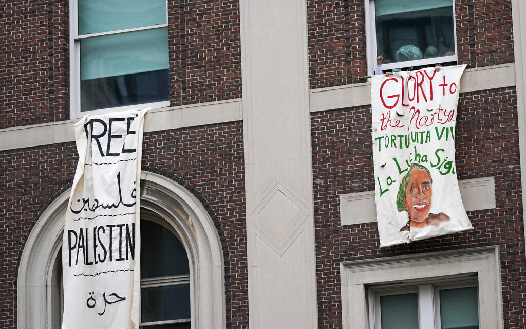 An anti-Israel demonstrator pumps his fist as he hangs a sign reading 'Glory to the Martyrs' from a window in Hamilton Hall inside the Columbia University campus, April 30, 2024, in New York. (AP Photo/Mary Altaffer)