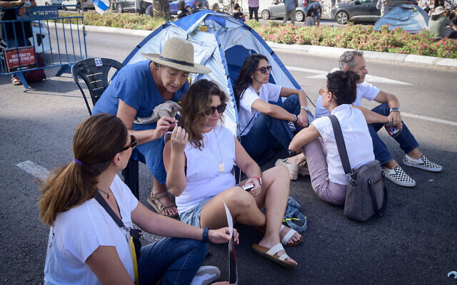 A woman passes a cigarette during a protest calling for the release of the people held  hostage by Hamas terrorists in Gaza, outside the Defense Headquarters in Tel Aviv, November 3, 2023. (Avshalom Sassoni/ Flash90)