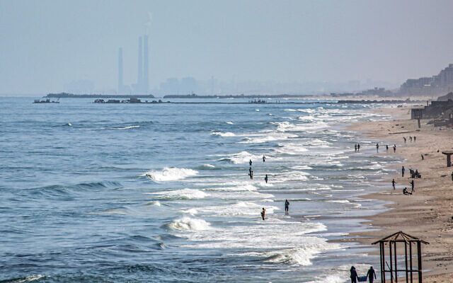 This picture, taken on May 16, 2024, shows people wading in the water of the Mediterranean Sea in the northern Gaza Strip, with Israel's Rutenberg power station near Ashkelon visible in the background. (Photo by AFP)