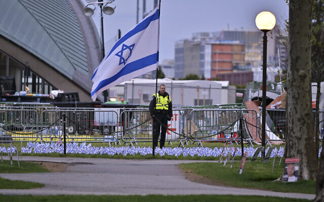 A police officer stands behind a display of Israeli flags beside the anti-Israel encampment that police raided and dismantled at MIT, before dawn on May 10, 2024, in Cambridge, Massachusetts. (AP Photo/Josh Reynolds)
