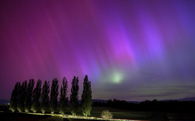 In this long exposure photograph, a car drives past and illuminates poplars as the northern lights glow in the night sky above the village of Daillens, Switzerland, early May 11, 2024. (Laurent Gillieron/Keystone via AP)
