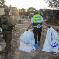 ZAKA volunteers walk through the destruction caused by Hamas terrorists in Kibbutz Kfar Aza, as they collect dead bodies, October 15, 2023. (Edi Israel/ Flash90)