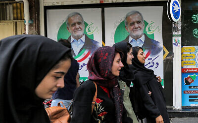 Women walk past election posters for Iranian reformist presidential candidate Massoud Pezeshkian along a street in Tehran on June 26, 2024 ahead of the vote. (RAHEB HOMAVANDI / AFP)