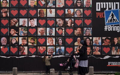 A woman and her children walk past a wall with photographs of hostages who were kidnapped during the October 7, 2023, Hamas cross-border attack in Israel, seen in Jerusalem, February 26, 2024. (Leo Correa/AP)