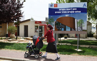A woman pushes a stroller as she walks past a placard indicating the location where a new cultural complex will be built, in the West Bank settlement of Beit El, May 1, 2019. (Gili Yaari /Flash90)