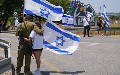 People outside Kibbutz Afik wave flags as they pay their last respects Sgt. Eyal Shynes, who was killed in Gaza, June 28, 2024. (Ayal Margolin/Flash90)