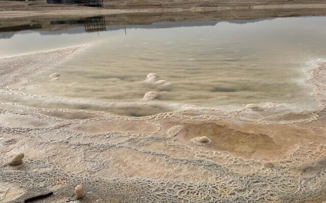 Salt formations on the southern coast of the Dead Sea, with the abandoned P88 pumping station in the background, and Masada on the horizon, May 28, 2024. (Sue Surkes/Times of Israel)