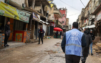 A man wearing a jacket bearing the logo of the United Nations Relief and Works Agency for Palestine Refugees (UNRWA), walks along a street devastated by the passage of Israeli military vehicles and bulldozers during raids, in the refugee camp of Balata in the West Bank on February 4, 2024. (Jaafar Ashtiyeh/AFP)