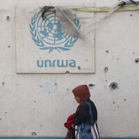 A Palestinian woman walks past a damaged wall bearing the UNRWA logo at a camp for internally displaced people in Rafah in the southern Gaza Strip on May 28, 2024. (Eyad Baba/AFP)