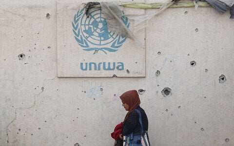 A Palestinian woman walks past a damaged wall bearing the UNRWA logo at a camp for internally displaced people in Rafah in the southern Gaza Strip on May 28, 2024. (Eyad Baba/AFP)