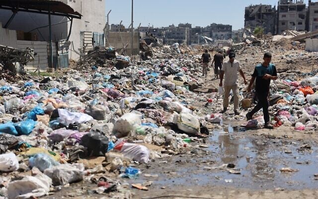 Palestinians walk past mounds of garbage and open sewage in the Sheikh Radwan neighborhood, north of Gaza City, on July 3, 2024 (Omar AL-QATTAA / AFP) Palestinians walk past mounds of garbage and open sewage in the Sheikh Radwan neighborhood, north of Gaza City, on July 3, 2024 (Omar AL-QATTAA / AFP)