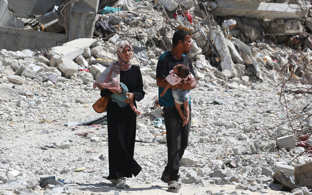 A Palestinian couple holds their children as they walk through debris in Khan Younis in the southern Gaza Strip on July 4, 2024 (Bashar TALEB / AFP)