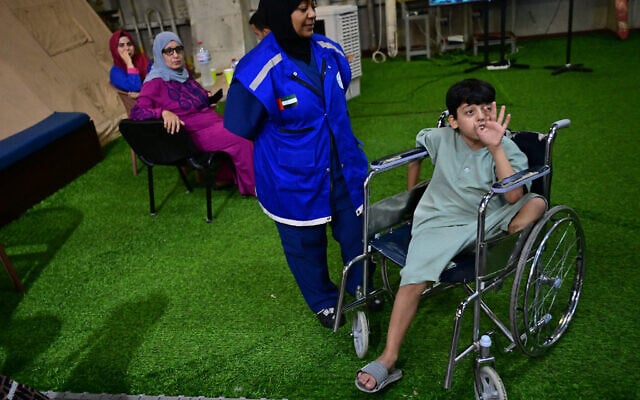 A young Palestinian amputee evacuated from the Gaza Strip sits in a wheelchair as a medic looks on, aboard an Emirati floating hospital in the Egyptian port of Al-Arish on July 4, 2024, during an organised press tour. (Photo by Giuseppe CACACE / AFP)