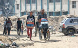 Palestinians walk with water and food through a heavily damaged residential district of the Gaza Strip's southern city of Khan Younis, July 5, 2024. (Bashar Taleb / AFP)