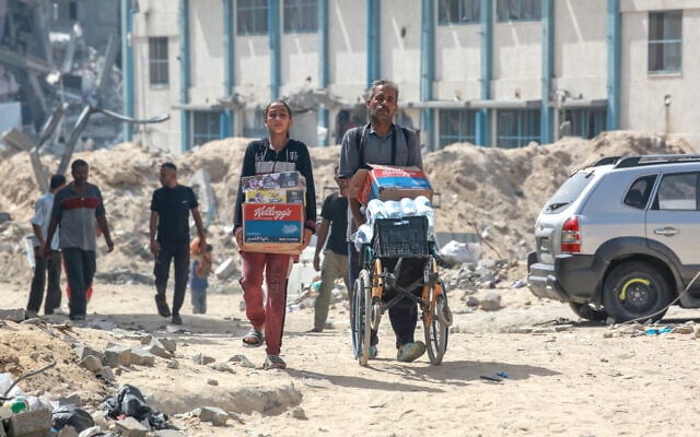 Palestinians walk with water and food through a heavily damaged residential district of the Gaza Strip's southern city of Khan Younis, July 5, 2024. (Bashar Taleb / AFP)