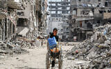 A boy pushes a wheelchair carrying water containers past the rubble of destroyed buildings along a street in Khan Younis in the southern Gaza Strip on July 8, 2024. (Bashar Taleb/AFP)
