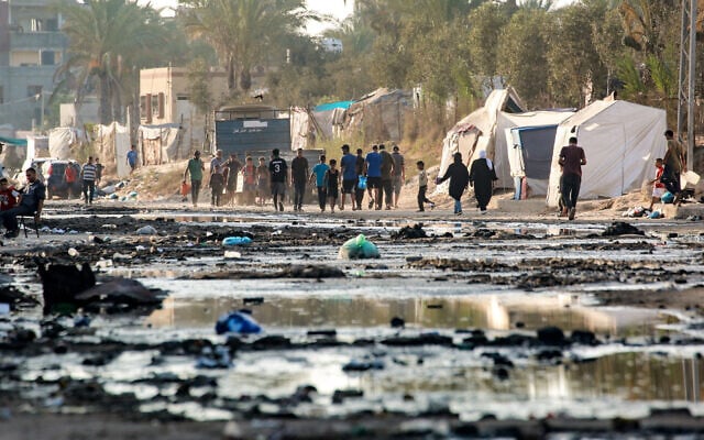 Palestinians walks near tents used as shelter along a street covered with stagnant wastewater in Deir al-Balah in the central Gaza Strip on July 19, 2024. (Bashar Taleb/AFP)