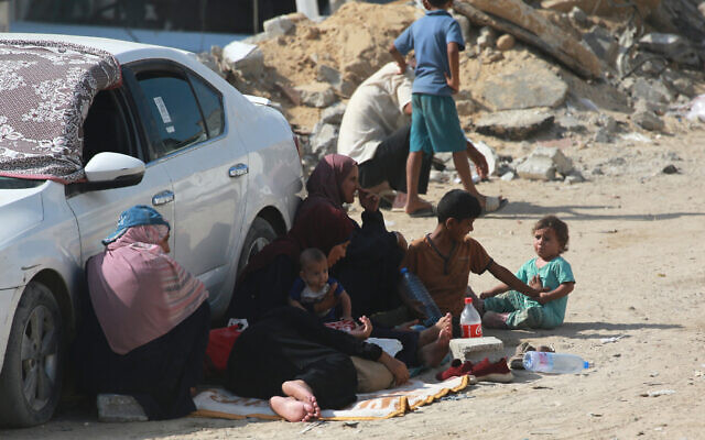 A Palestinian family rests is the shade of a vehicle parked near the rubble of a building, as thousands of Palestinians who fled following the Israeli army's temporary evacuation order for parts of Khan Younis arrive in an another area of the southern Gaza Strip city on July 23, 2024 (Bashar TALEB / AFP)