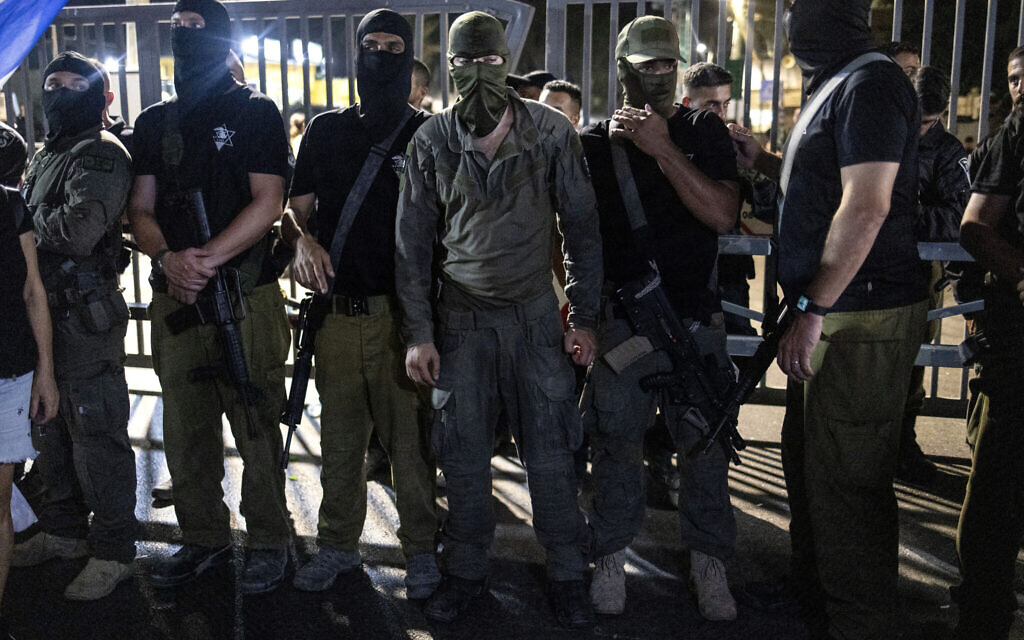 Far-right demonstrators, some of them wearing military uniforms and face masks and carrying weapons, gather outside the Beit Lid army base as they protest over the detention for questioning of military reservists who are suspected of abuse of a Palestinian terror suspect detained there, on July 29, 2024. (Oren Ziv / AFP)