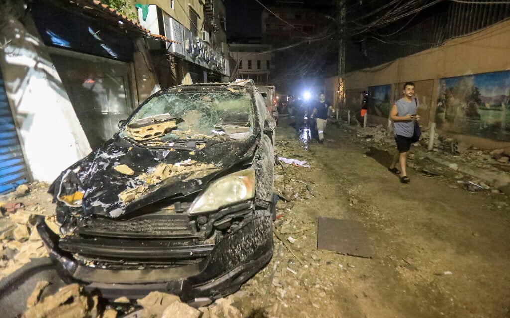 Men walk past debris and a destroyed car after the top floors of an eight-story building were destroyed following an Israeli military strike in a Beirut's southern suburb, on July 30, 2024. (AFP)