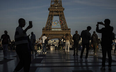 People use their smartphones near the Olympic rings that are displayed on the Eiffel Tower in Paris, June 7, 2024 in Paris. (AP Photo/Aurelien Morissard, File)
