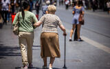 A caregiver walks with an elderly woman on Jaffa Street in downtown Jerusalem on July 2, 2023. (Nati Shohat/Flash90)