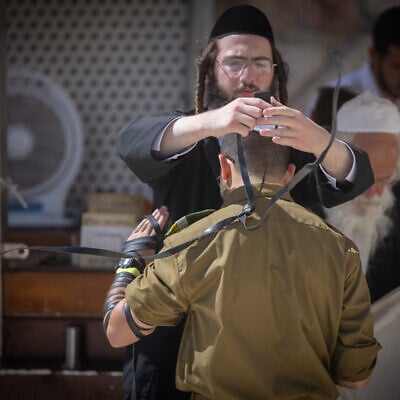A Haredi man places tefillin on a soldier  in the Old City of Jerusalem, June 25, 2024. (Chaim Goldberg/Flash90)
