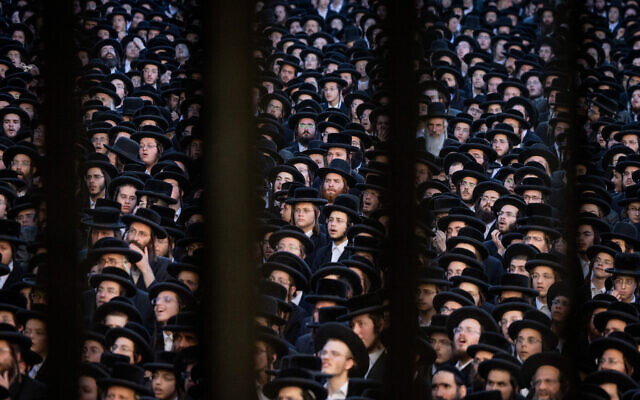 Thousands of ultra-Orthodox -- photographed here through a metal fence -- attend a rally against the conscription of Haredi yeshiva students to the military, in Jerusalem's Mea Shearim neighborhood on June 30, 2024. (Chaim Goldberg/Flash90)