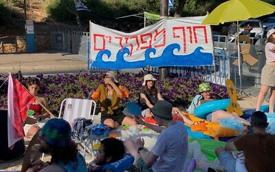 Anti-government demonstrators protest outside the Knesset building in Jerusalem under banner that reads 'Abandoners' Beach,' criticizing the three-month legislative recess that began the same day, on July 28, 2024. (Charlie Summers/Times of Israel)