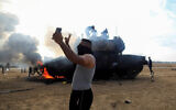 Gazans at a burning Israeli military vehicle on the Israeli side of the Israel-Gaza border, October 7, 2023. (REUTERS/Yasser Qudih)