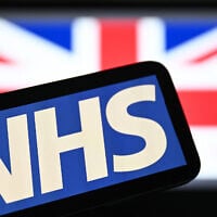 An illustration taken on July 7, 2024, shows the National Health Service (NHS) logo displayed on a screen backdropped by the Union Jack flag. (JUSTIN TALLIS / AFP)