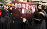 An Iranian woman at Hamas political leader Ismail Haniyeh's funeral procession in Tehran holds a sign showing terror leaders and a nuclear scientist whose deaths have been blamed on Israel, August 1, 2024. These are (L to R) Palestinian Islamic Jihad secretary general Fathi Shaqaqi, Iranian physicist and scientist Mohsen Fakhrizadeh, Iraqi commander Abu Mahdi al-Muhandis, Haniyeh, Iranian Quds Force chief Qasem Soleimani, Hezbollah commander Imad Mughnieh and Hamas spiritual guide Sheikh Ahmed Yassin. (AFP)