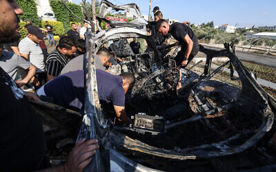 People check a car attacked in an IDF airstrike in the West Bank city of Tulkarem, August 3, 2024. (Jaafar Ashtiyeh/ AFP)
