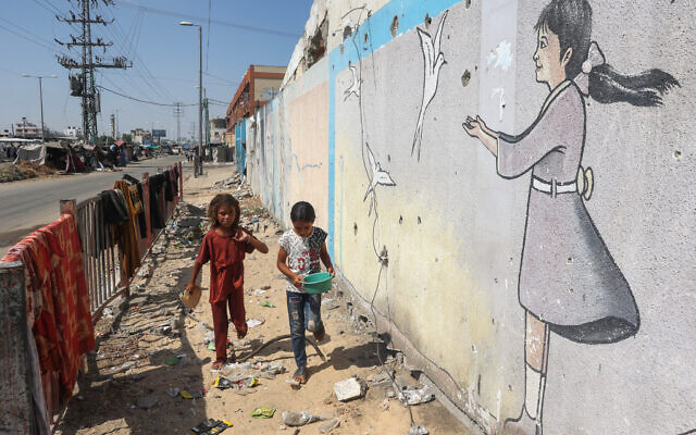 Palestinian children walk past a mural at a makeshift displacement camp set up on a roadside in Deir el-Balah in the central Gaza Strip on August 13, 2024 (Eyad Baba/AFP) Palestinian children walk past a mural at a makeshift displacement camp set up on a roadside in Deir el-Balah in the central Gaza Strip on August 13, 2024 (Eyad Baba/AFP)