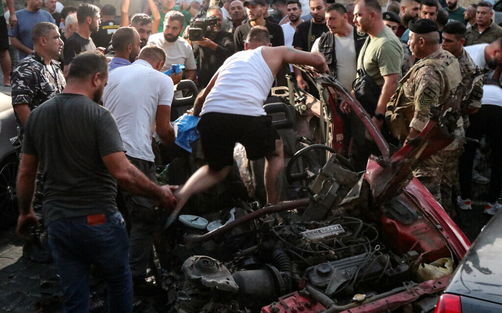 People and security forces check the wreckage of a car, reportedly targeted by an Israeli drone attack in the main square of the southern Lebanese town of Marjayoun on August 14, 2024, amid ongoing cross-border tensions between Israel and Hezbollah fighters. - The Lebanese health ministry said in a statement that the Israeli strike in Marjayoun killed at least two people and wounded four others. (Photo by Rabih DAHER / AFP)