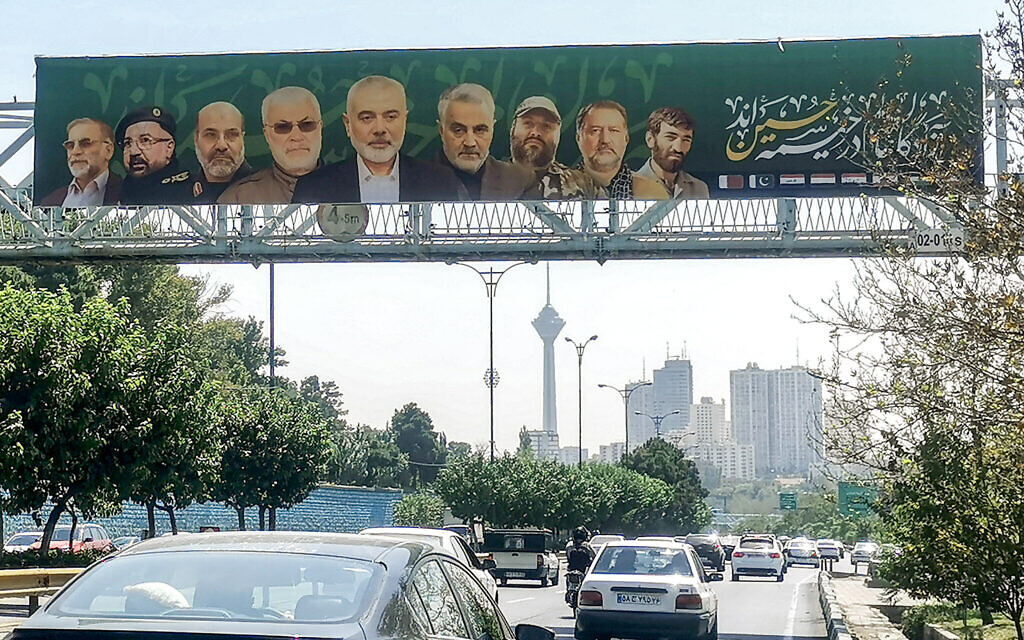 Vehicles move along a road underneath a pedestrian overpass with a large banner depicting the slain commander of the Islamic Revolutionary Guard Crops' (IRGC's) Quds Force Qassem Soleimani, fourth from right, and slain figures of Iran-backed groups, including Hamas' Ismail Haniyeh, center, in Tehran on August 14, 2024. (ATTA KENARE / AFP)