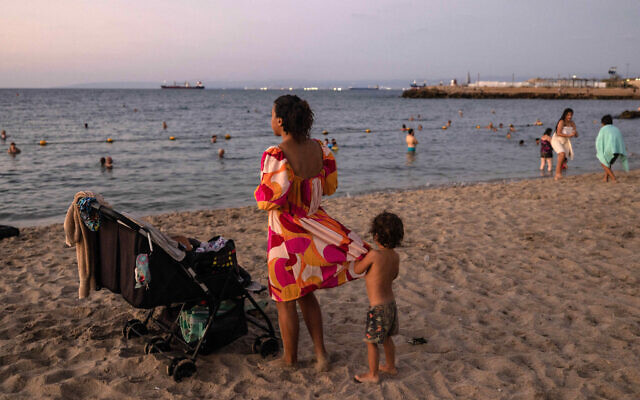 Illustrative: A woman accompanied by children stares at the Mediterranean sea in Israel's northern coastal city of Haifa on August 14, 2024. (MENAHEM KAHANA / AFP)
