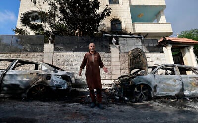 A man stands in front of burnt cars, a day after an attack by Jewish settlers on the village of Jit near Nablus in the occupied West Bank that left a 23-year-old man dead and others with critical gunshot wounds, on August 16, 2024. (Jaafar Ashtiyeh / AFP)