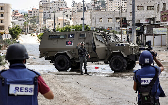 Journalists film Israeli army vehicles deployed at the entrance of Tulkarem , during an ongoing raid, in the West Bank on August 22, 2024. (Zain JAAFAR / AFP)