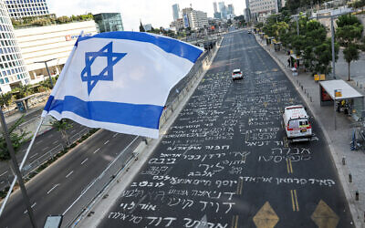 This overview shows an Israeli flag flying from a pedestrian bridge above a road inscribed with the names of hostages captive in the Gaza Strip since the October 7 attacks inscribed in Hebrew, outside the Israeli Defense Ministry headquarters in Tel Aviv on August 24, 2024. (Jack GUEZ / AFP)