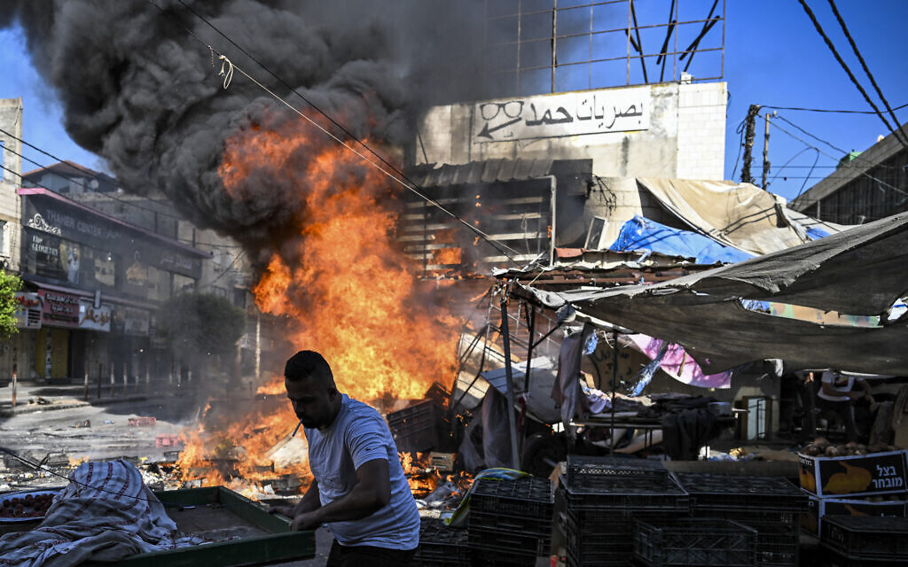 A Palestinian man collects salvageable items as a fire breaks out in a fruit market in the West Bank city of Jenin during ongoing Israeli raids on August 31, 2024. (RONALDO SCHEMIDT / AFP)