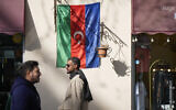 People pass by a flag on the wall in Baku, Azerbaijan, Monday, February 5, 2024. (AP Photo/Sergei Grits)